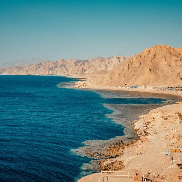 Rocky coastline with blue sea and mountains.