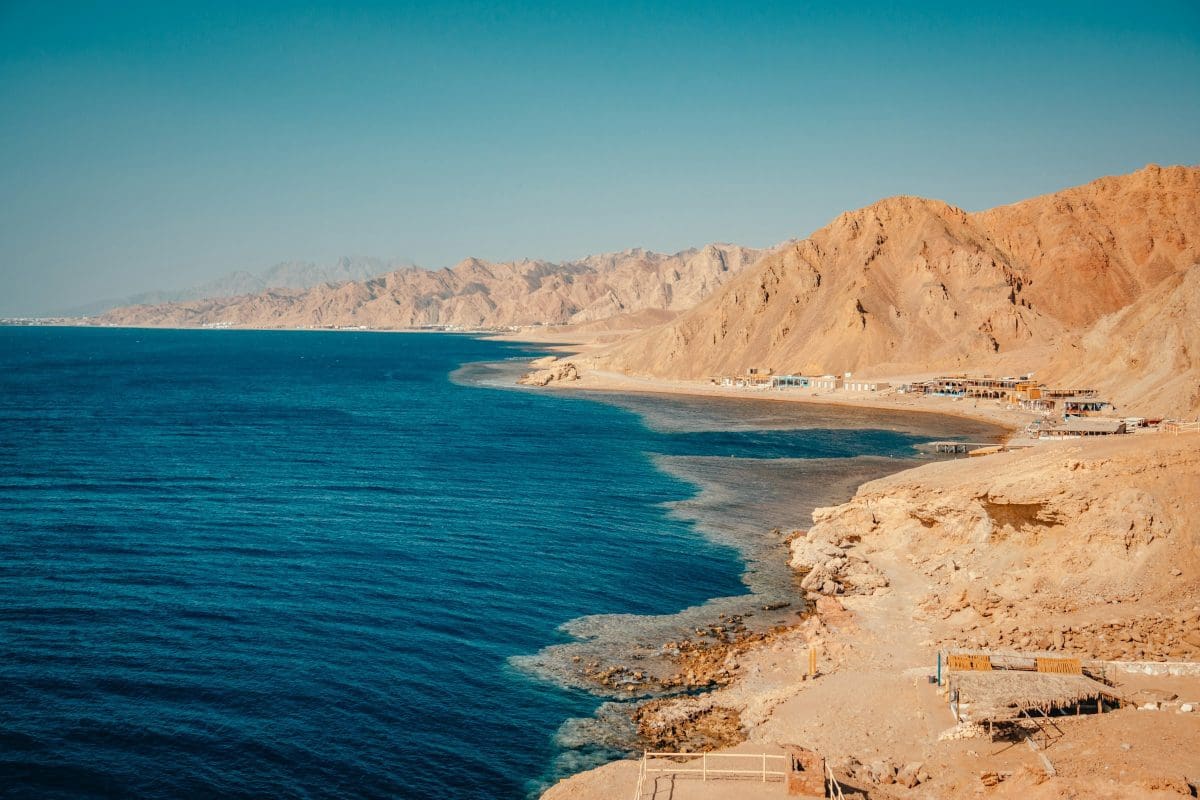 Rocky coastline with blue sea and mountains.