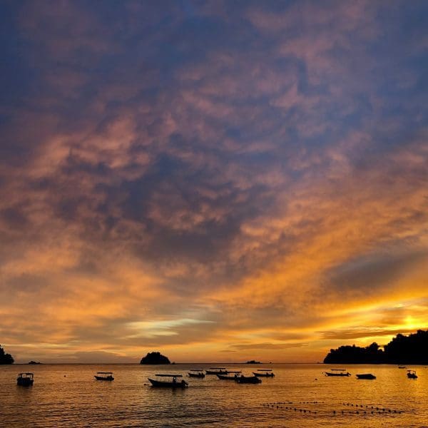 Sunset over sea with boats and clouds.