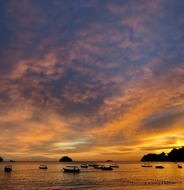 Sunset over sea with boats and clouds.
