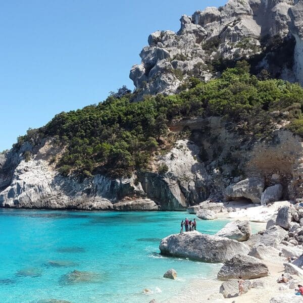 Turquoise sea with rocky cliffs and beachgoers.