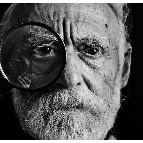 Elderly man with magnifying glass over eye, black and white.