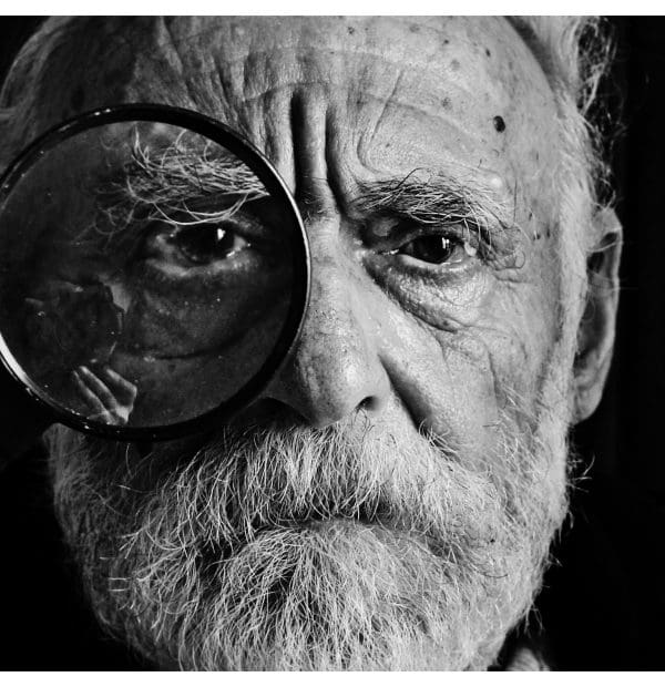 Elderly man with magnifying glass over eye, black and white.