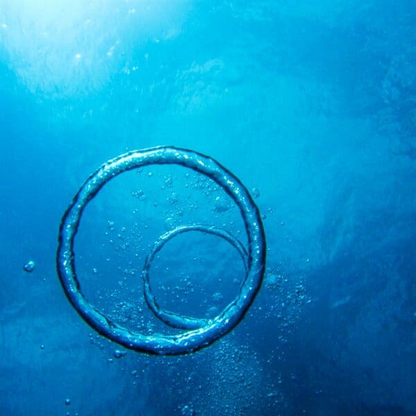 Underwater air bubble ring ascending in blue ocean waters.
