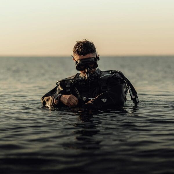 Scuba diver adjusting gear in tranquil sea at sunset.
