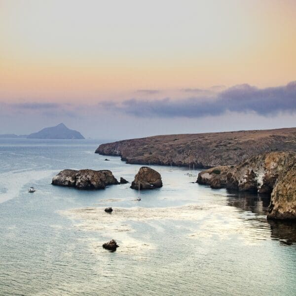 Coastal sunset over serene bay with cliffs and boats.