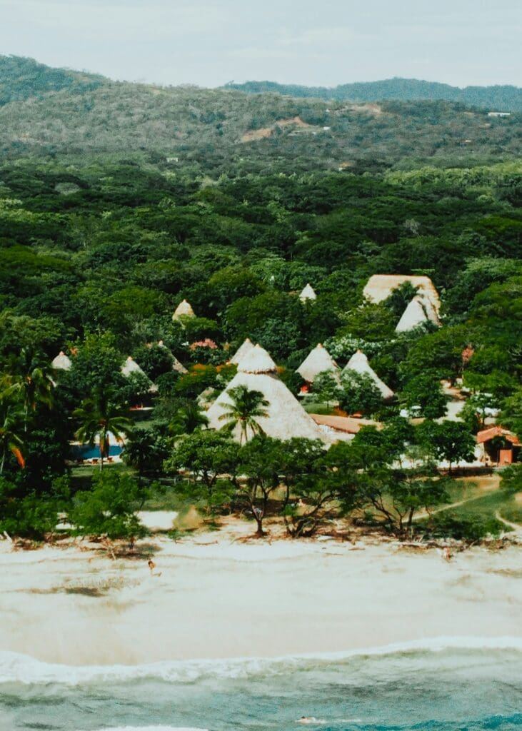 Tropical beach resort with thatched roof bungalows and lush hills