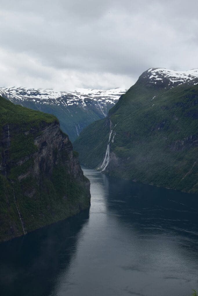 Fjord with waterfall surrounded by snow-capped mountains