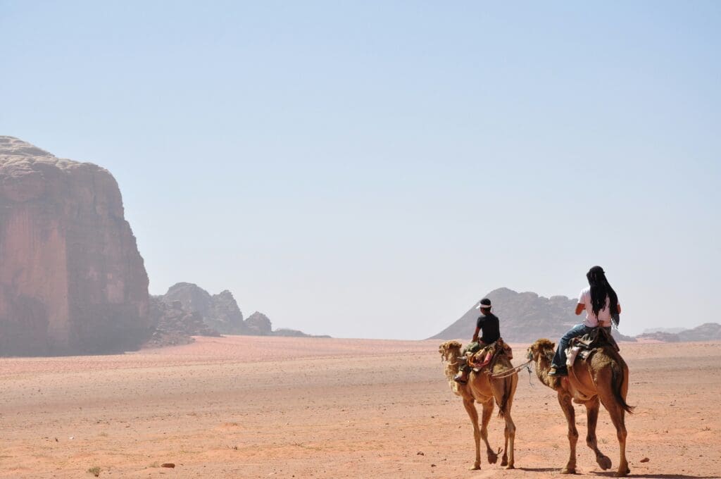 Two people riding camels in a desert landscape