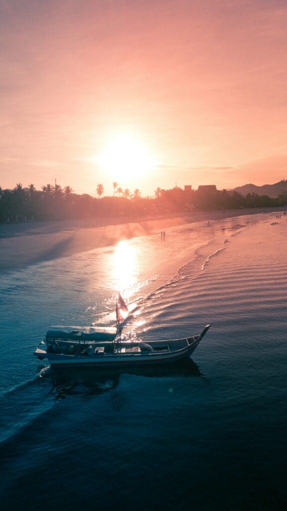 Sunset over beach with boat and palm trees