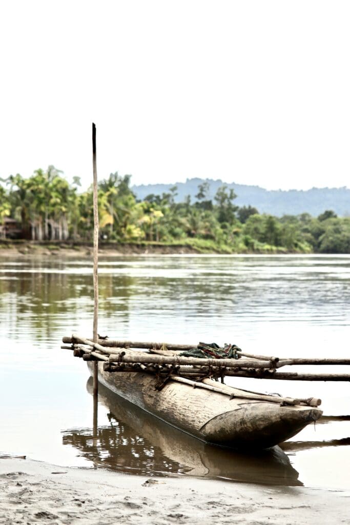 Traditional wooden canoe on riverbank with lush background