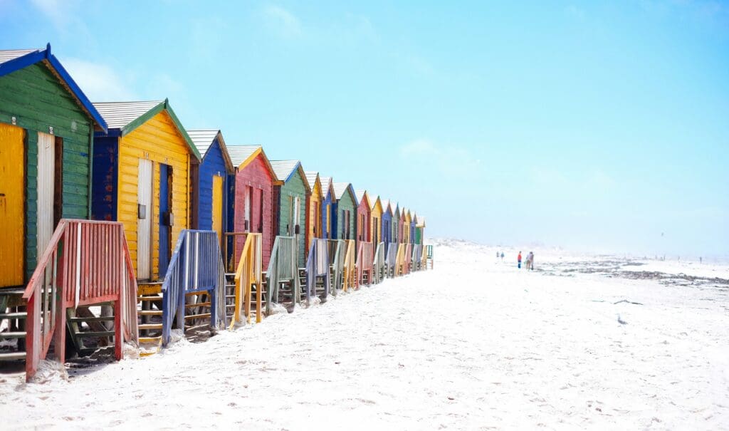 Colorful beach huts on sandy shore with people walking