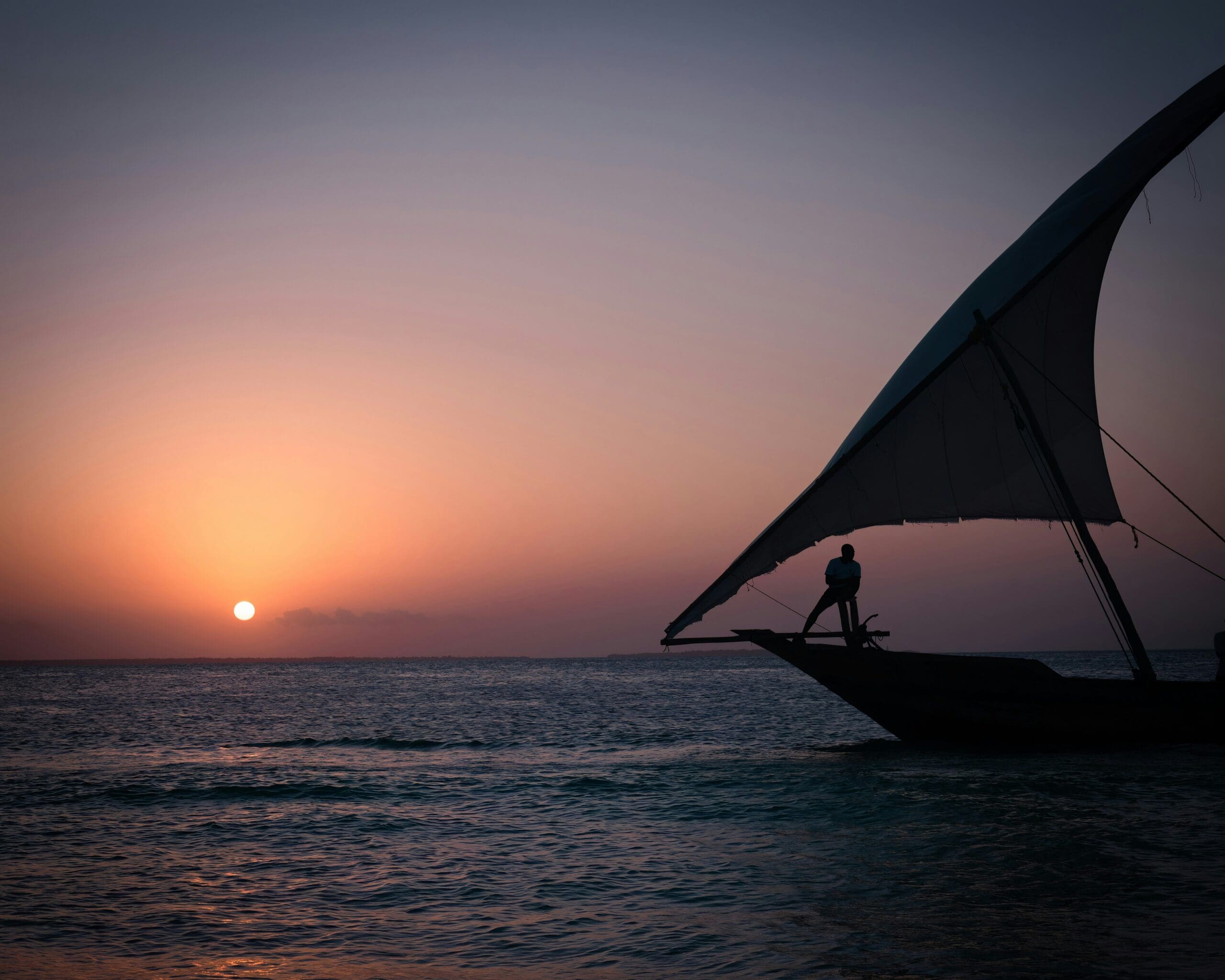 Silhouetted sailboat at sunset on serene sea