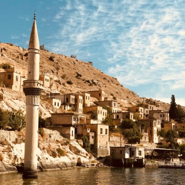 Old village and minaret by a river under blue sky